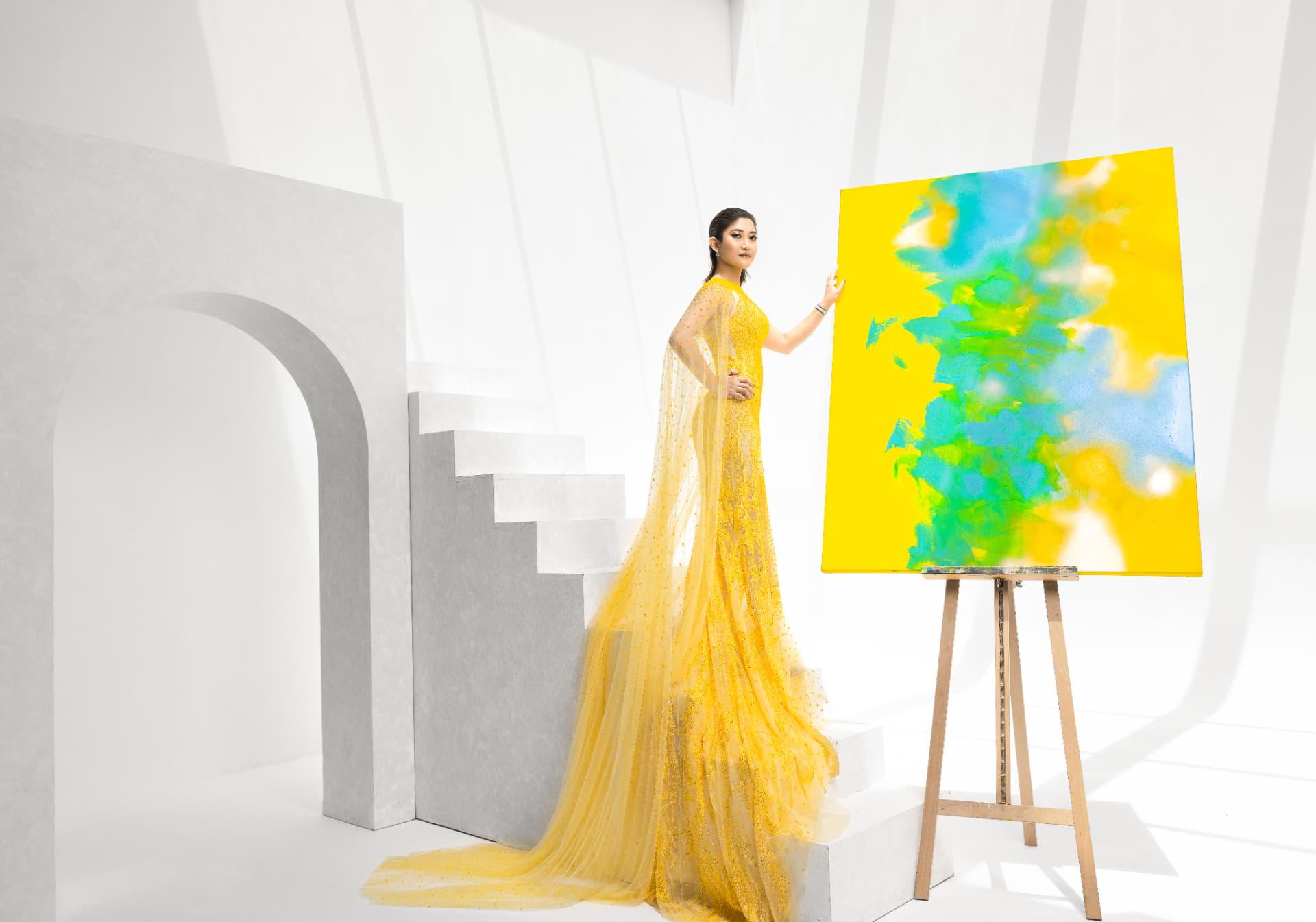 Romina May in a yellow gown beside a new painting on an easel